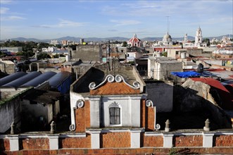 Mexico, Puebla, View across city rooftops with part view of red brick and white building facade in