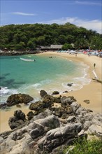 Mexico, Oaxaca, Puerto Escondido, View onto Playa Manzanillo beach with rocks in foreground and