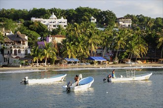Mexico, Oaxaca, Puerto Escondido, Fishing boats in bay at Playa Marinero lined with cafes bars and