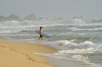 Mexico, Oaxaca, Puerto Escondido, Surfer walking into surf carrying board. Photo : Nick Bonetti