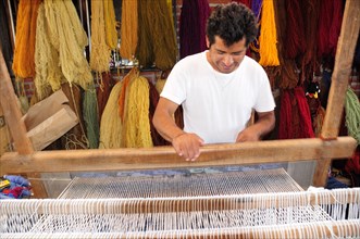 Mexico, Oaxaca, Teotitlan del Valle, Weaver at loom with different coloured yarn hanging in bundles
