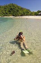 Mexico, Oaxaca, Huatulco, Snorkler adjusting mask while sitting in clear water beside Playa La