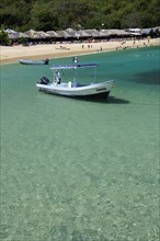 Mexico, Oaxaca, Huatulco, Playa La Entrega Tour boat moored in clear shallow water in foreground of