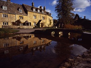 England, Gloucestershire, Cotswolds, Lower Slaughter. Village houses reflected in the River Eye.