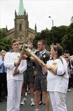 England, Kent, Tunbridge Wells, Olympic Torch relay runners handing over torch by exchanging the