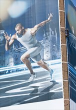 England, London, Stratford A man suspended by rope secures giant hoarding of Gymnast Louis Smith to