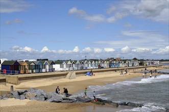England, Suffolk, Southwold, Beach Huts near the pier with Sea Defences and Holidaymakers. Photo :