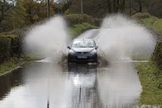 England, Kent, Flooding, Flooded country road with cars driving slowly through waters. Photo : Sean