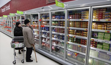 Shopping, Supermarket, Food, Elderly couple with shopping trolley looking at frozen goods in glass