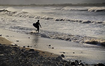 Ireland, County Sligo, Strandhill, Silhouette of surfer with surfboard heading into the sea. Photo