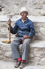 Nepal, Upper Mustang, Lo Manthang, Elderly man praying with prayer wheel in the square near the