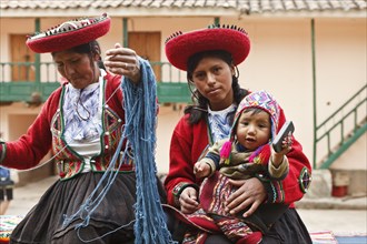Peru, Indigenous People, Mother and baby in traditional dress with a lady making yarn and infant