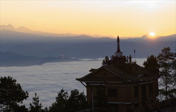 Nepal, Nagarkot, Sunrise view across clouded valley towards Himalayan mountains with Buddhist Stupa