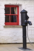 Ireland, North, Derry, Craft Village, Old water pump with small red window in background. 
Photo