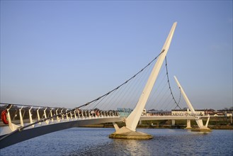 Ireland, North, Derry, The Peace Bridge over the River Foyle opened in 2011 with the former Ebrington Barracks in the background.