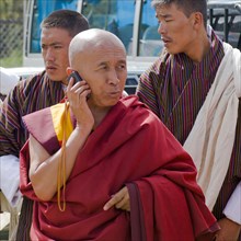 Bhutan, , Red robed Tibetan Buddhist monk talking on his mobile phone. 
Photo Nic I'Anson
