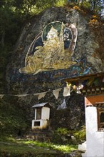 Bhutan, Thimpu, Gold painted carving of Guru Rimpoche on rock wall.