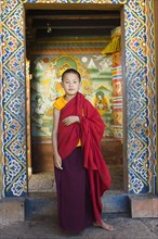 Bhutan, Chimi Lakhang, Young novice monk standing in doorway of Chimi Lakhang temple in the old
