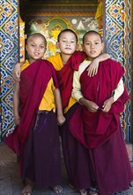 Bhutan, Punakha, Three young novice monks standing in doorway of Chimi Lakhang temple in the old