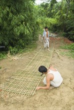 Bangladesh, Chittagong Division, Khagrachari, Two men weaving a large bamboo fence panel. 
Photo