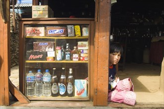 Nepal, Himalayas, Pokhara, Girl sat in a shop doorway on a trekking route with western snacks for