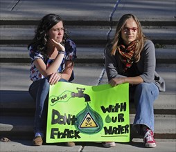 Canada, Alberta, Lethbridge, Two local women atsitting on stone steps at an anti-fracking demonstration holding a green protest sign. Oldman River  which runs through Lethbridge  is the source of the ...