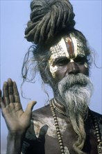 Portrait of Sadhu with painted face and hand raised, Kathmandu Valley, India.