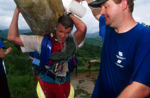 guy pours jug of water over another carrying a canoe