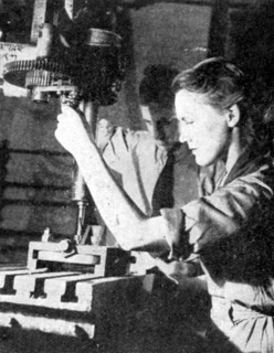 Woman in tank factory being instructed in the use of a metal power drill