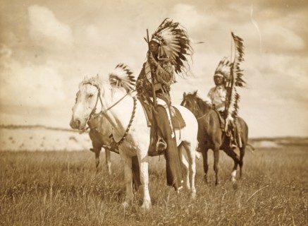 Three Native American chiefs mounted on horses and wearing feather headdresses