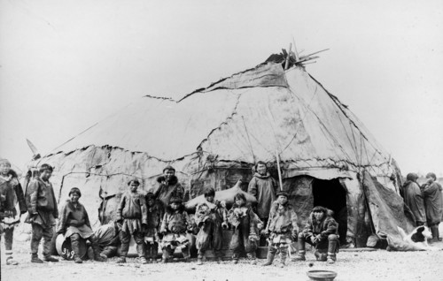 Native American men and children standing in front of a large tent structure