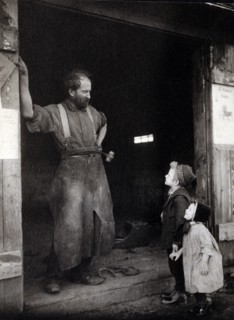 two children talking to a blacksmith standing in the doorway of his forge.