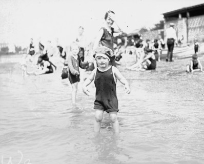 Young child at the edge of a beach crying as his family look on