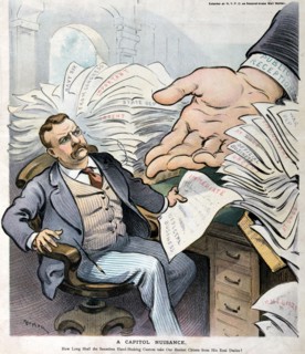 President Theodore Roosevelt sitting at a desk that is overwhelmed with papers