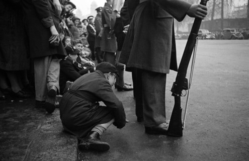 Child peers through legs to catch Princess Elizabeth's wedding.