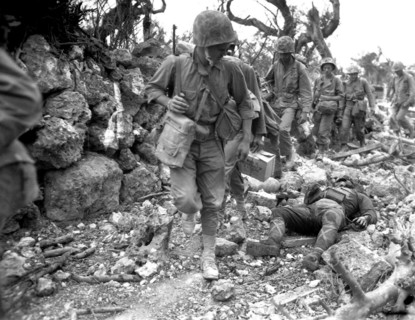 Photograph of Okinawa U.S. Marines pass a dead Japanese soldier in a destroyed village