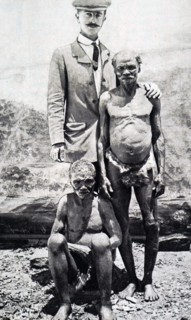Photograph of a member of a pigmy tribe, standing with a European visitor