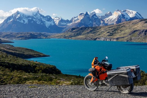 A heavily packed motorcycle on a gravel road behind the Lago del Torro and the mountain group Cordillera Paine