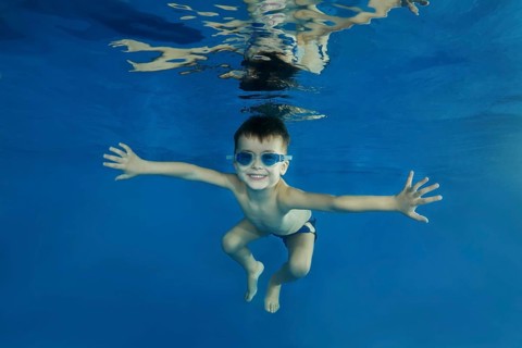 Young boy wearing swimming goggles dives in a pool