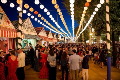 Spaniards celebrating in traditional clothes in front of lit marquees
