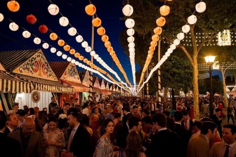 Spaniards celebrating in traditional clothes in front of lit marquees