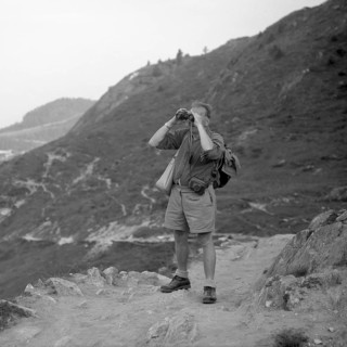 Man standing on a mountain path looking through binoculars