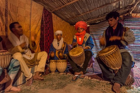 Bedouins with traditional clothes play on drums in a tent