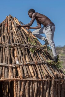 Man of the people of Ovahimba or Himba builds on the roof of a wooden hut