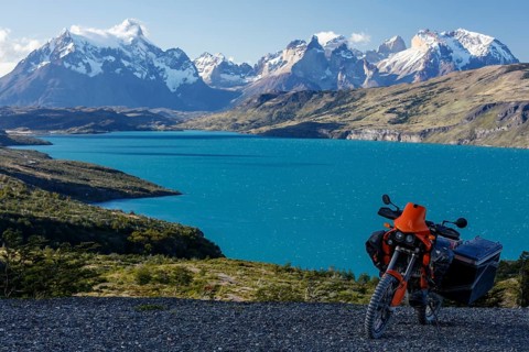 A heavily packed motorcycle on a gravel road behind the Lago del Torro and the mountain group Cordillera Paine