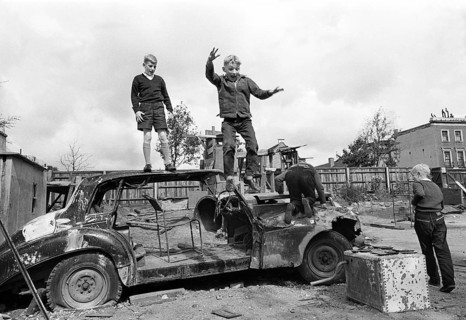 Three children play with car wreckage
