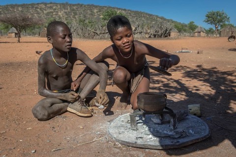 Children of the Ovahimba or Himba people look curiously into a pot over the fire