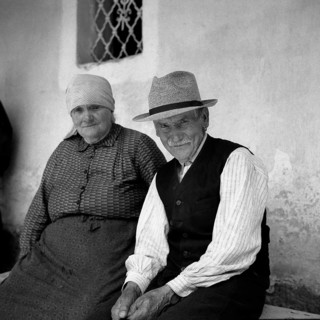 Old couple sitting on a bench and smiling at the camera