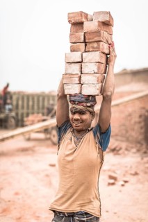 Worker with bricks on his head in the brickyard