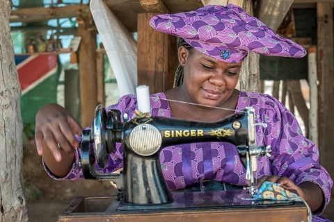 Native Herero woman with typical headgear and clothes is sitting at a sewing machine
